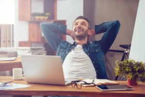 Hombre sonriendo frente a una computadora, experimentando un momento de felicidad y bienestar personal